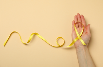 Hand holding a yellow endometriosis awareness ribbon on a beige background